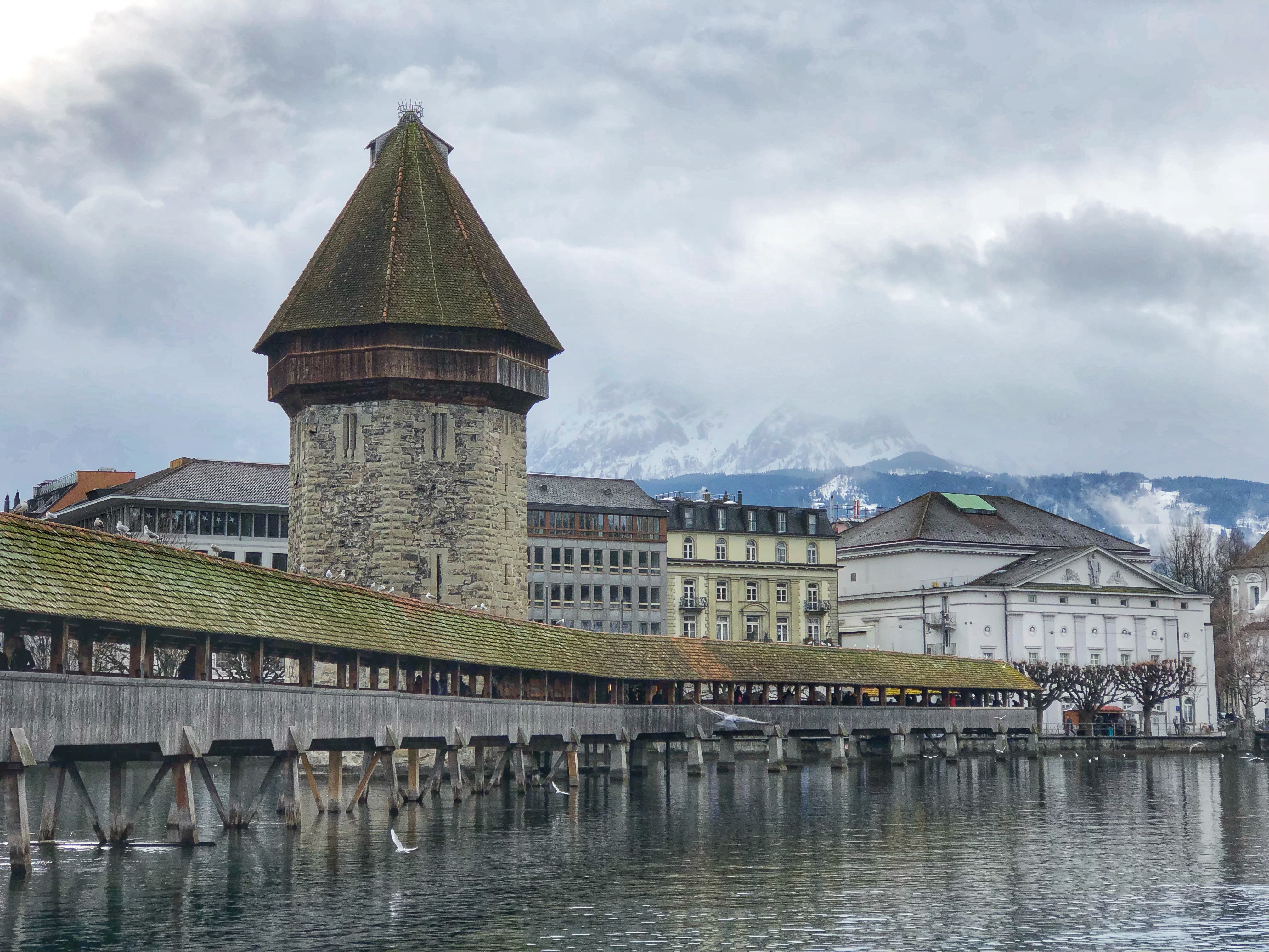 The Kapellbrücke, a wooden footbridge in Lucerne, Switzerland, with snowcapped mountains in the background.